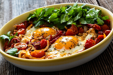 Shakshuka - fried eggs with vegetables on wooden table	