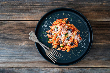 Penne noodles with tomato sauce, black olives and parmesan cheese served on wooden table	