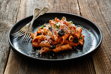 Penne noodles with tomato sauce, black olives and parmesan cheese served on wooden table	