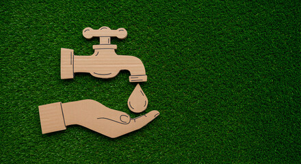 Cardboard Tap with Water Drop on a Hand Placed on Green Grass Backdrop Symbolizing Water Conservation