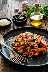 Penne noodles with tomato sauce, black olives and parmesan cheese served on wooden table	