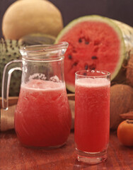 Watermelon juice glass jug on tropical fruits background.