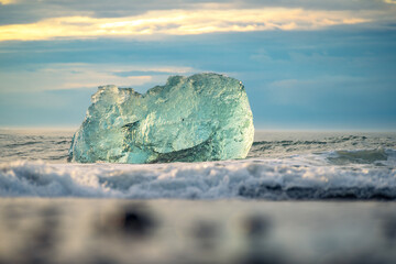 Sunrise light shines through a crystal clear ice chunk on the black sand beach by Jokulsarlon...