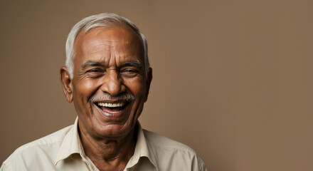 Laughing senior man with white mustache and beard against beige background. Joyful aging and positive attitude concept for elderly wellbeing campaigns