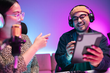 Teenagers, men and women, host podcasts in a room using LED lights, computers, headphones, condenser microphones, and tablets to share their knowledge and experiences through live online broadcasts.