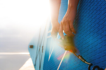 Female hands of young Caucasian woman fastening leash on paddle board at sunset