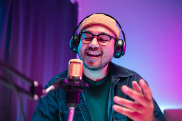 Teenagers, men and women, host podcasts in a room using LED lights, computers, headphones, condenser microphones, and tablets to share their knowledge and experiences through live online broadcasts.