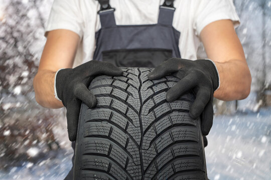 Car mechanic with winter tire. Snowing in background.