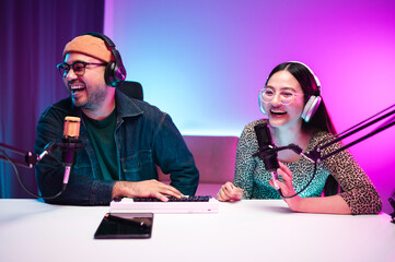 Teenagers, men and women, host podcasts in a room using LED lights, computers, headphones, condenser microphones, and tablets to share their knowledge and experiences through live online broadcasts.