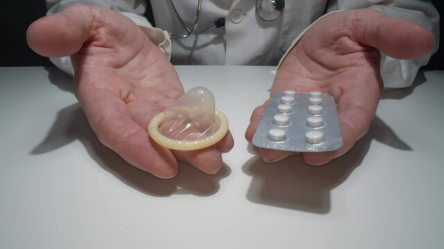 Doctor is holding consom and pills in hands. Comparison of contraception. Concept of healthcare and medicine.