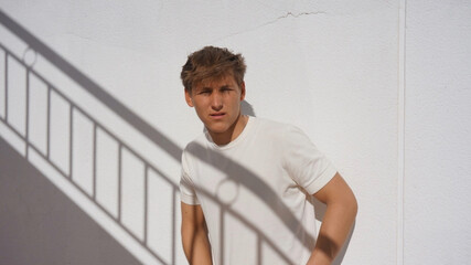 Young man leaning on white wall outdoor, shadow of stairs on him