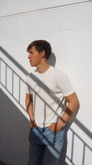 Young man leaning on white wall outdoor, shadow of stairs on him