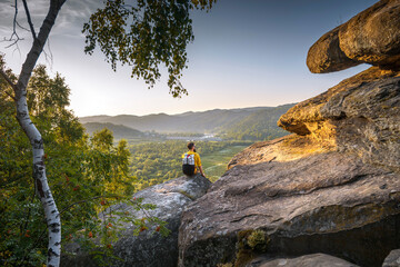 Bearded backpacker hiker sitting on rocky terrain in the mountains, gazing at the valley with a...