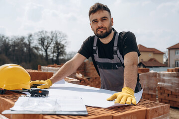 Positive facial expression, standing. Construction worker is at job with bricks outdoors