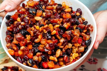Close-up of a bowl filled with assorted dried fruits held gently by two hands.