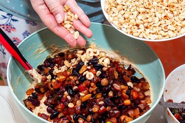A close-up shot of a hand pouring nuts into a bowl of mixed fruits for baking.