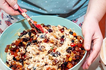 Close-up shot of a person mixing fruit and nuts into a cake batter in a large bowl.