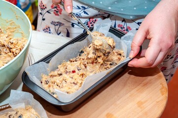Hands carefully filling a loaf pan with fresh fruitcake batter in preparation for baking.