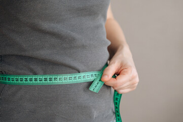 Woman measuring her waist with green measuring tape. Weight loss, healthy lifestyle concept. 