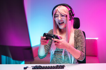 A young female streamer is happily playing a game, smiling looking very determined in a room lit...