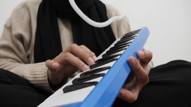 Asian muslim woman wearing hijab playing pianica, melodica blow organ