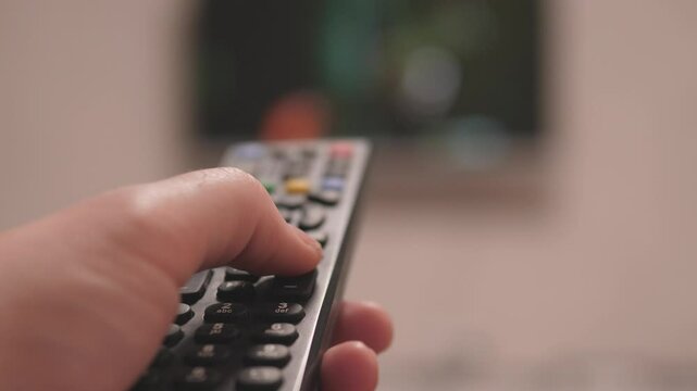A hand skillfully operating a remote control, pointing at a bright television screen while enjoying entertainment