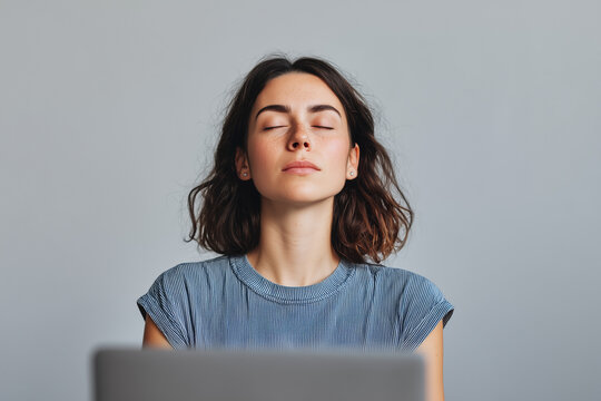 Young woman meditating at office desk with closed eyes
