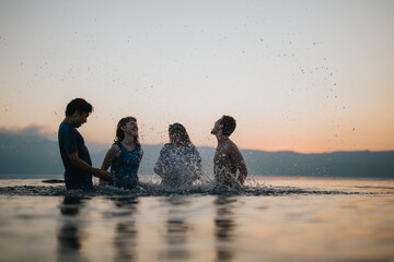 A group of friends splashing and laughing in a serene lake during sunset, enjoying the warm evening and creating joyful memories together.