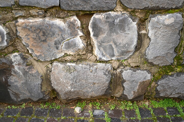 Rough stone wall displays various gray hues with patches of moss,