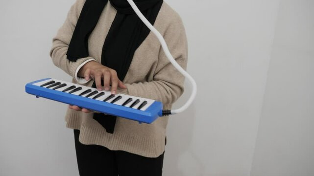 Asian muslim woman wearing hijab playing pianica, melodica blow organ