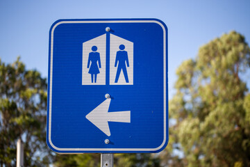 a blue and white public restroom (toilet) sign with a left-pointing arrow. The sign features the traditional male and female symbols.
