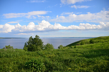 Fototapeta premium Scenic view of a green hillside, water and sky with chain of cumulous clouds
