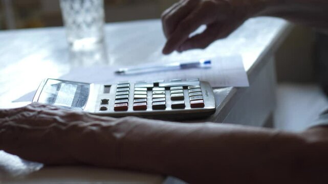 Retiree calculating expenses and income on calculator, hands of elderly man pressing calculator buttons and writing payment documents, senior family budget