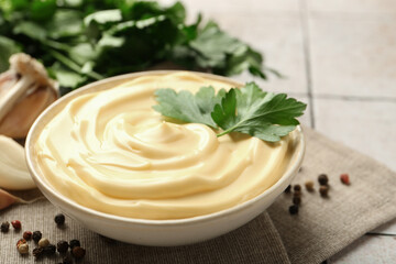 Delicious mayonnaise sauce with parsley in bowl on tiled table, closeup