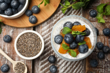 Delicious chia pudding with blueberries, peaches and mint in glass on wooden table, flat lay
