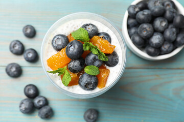 Delicious chia pudding with blueberries, peaches and mint in glass on light blue wooden table, flat lay