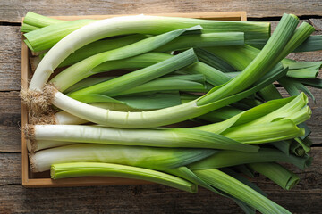 Fresh leeks in crate on wooden table, top view