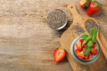 Delicious chia pudding with strawberries and mint in jar on wooden table, flat lay. Space for text