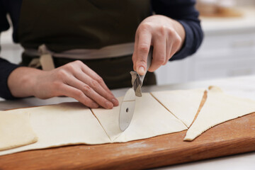 Woman cutting dough at light table indoors, closeup. Making croissants