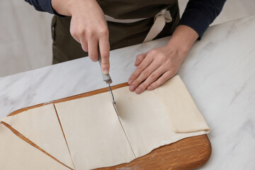 Woman cutting dough at light marble table, closeup. Making croissants