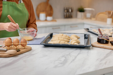 Woman whisking egg wash near raw croissants at white marble table in kitchen, closeup