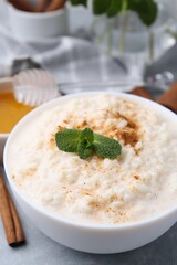 Tasty rice pudding with cinnamon, mint and honey on light grey table, closeup