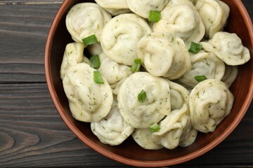 Tasty dumplings with green onion and dill in bowl on wooden table, top view