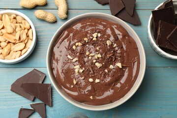 Tasty chocolate pudding in bowl and ingredients on light blue wooden table, flat lay