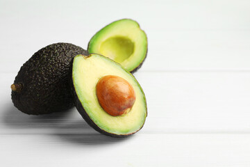 Whole and cut avocados on white wooden table, closeup. Space for text