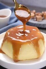 Pouring caramel sauce onto pudding on table, closeup