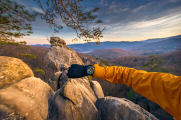 POV: a human arm showing a Casio wristwatch on top of a mountain while taking a break. In the...