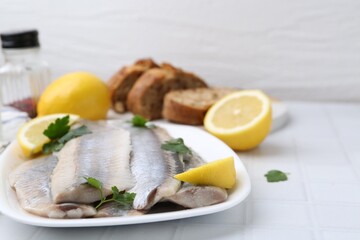 Marinated herring fillets with lemon and parsley on white tiled table, closeup. Space for text