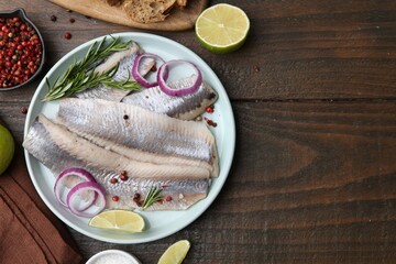 Marinated herring fillets with onion rings, rosemary, lime and spices on wooden table, flat lay....