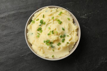 Delicious mashed potato with green onions in bowl on black table, top view